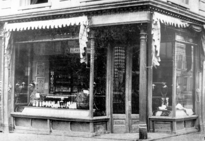 Drug store with large picture windows on the front and a recessed doorway. Displays are in the windows and drapery hangs above them.