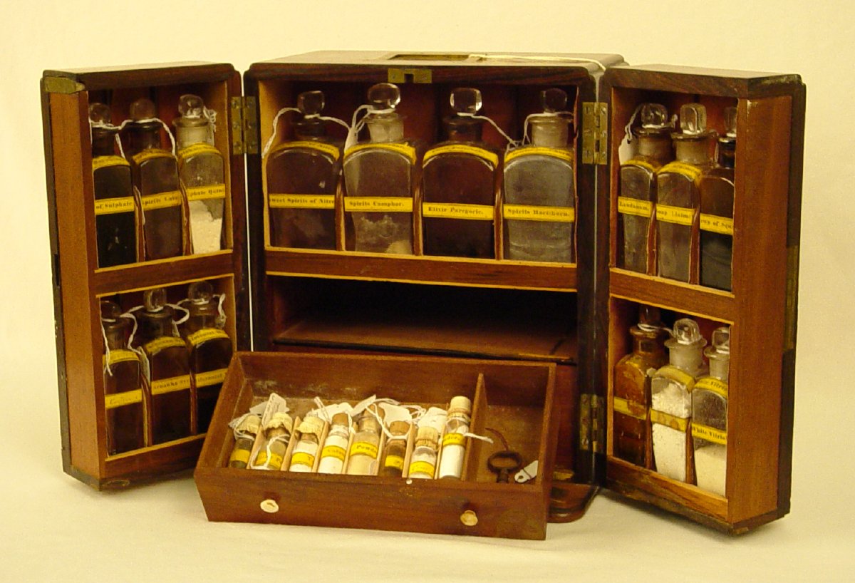 Wooden chest with two doors. Inside the doors and the interior are clear glass bottles full of medicine. There are two drawers inside and one is open, showing tiny medicine vials full of substances.