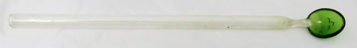 Clear glass medicine spoon with green scoop portion with a cross embossed in it.